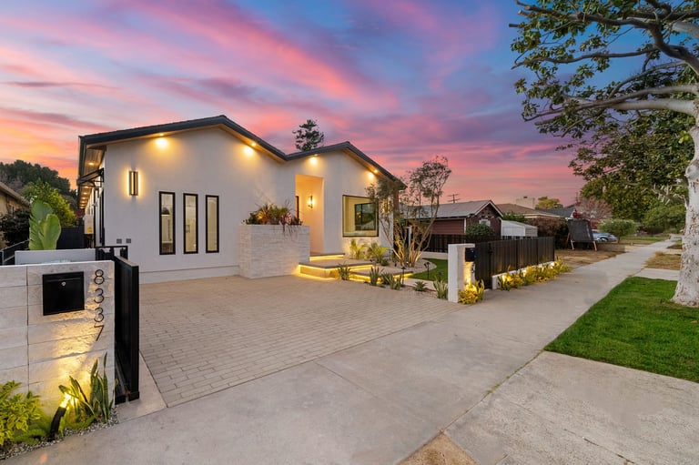 Modern house exterior with illuminated facade and landscaped front yard at sunset